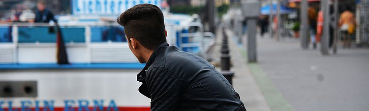 Ein junger Mann sitzt auf einer Mauer und schaut in die Ferne