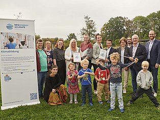 Gruppenbild der Kita-Leitung Moosstiege mit Kindern der Kita und der Auszeichnung zur KlimaKita.NRW.