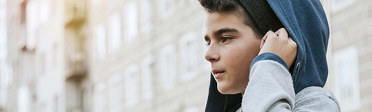 Ein Junge mit Migrationshintergrund steht vor einer Häuserfassade