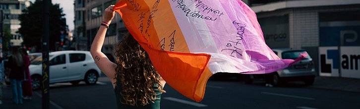 Eine Frau läuft mit einer wehenden bunten Flagge an einer Straße entlang