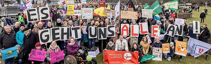 Eine große Menschenmenge hält verschiedene Plakate in die Höhe und formt mit Schildern den Schriftzug "Es geht uns alle an!"