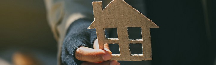 Eine Person hält ein Haus aus Pappe in der Hand