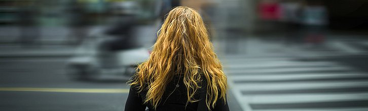 Nur von hinten zu sehende Person mit langen Haaren steht am Straßenrand