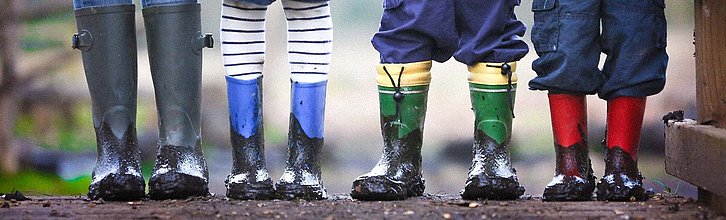 Vier Kinder stehen mit dreckigen Gummistiefeln nebeneinander