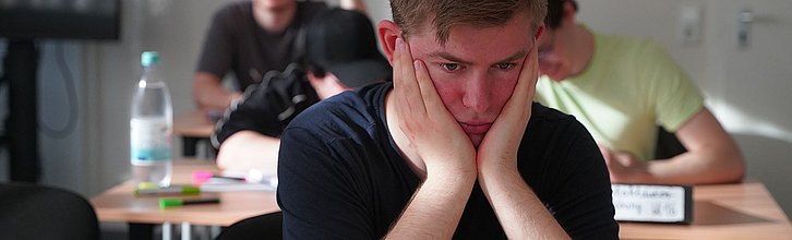 Eine junge Person in einem Klassenzimmer stützt den Kopf in seine Hände