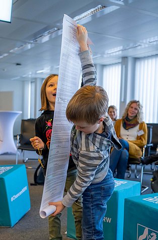 Zwei Kinder präsentieren eine lange Rolle aus bedrucktem Papier.