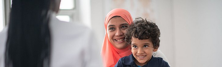 Eine Person mit einem Kind auf dem Schoß unterhält sich mit einer ihr gegenüber sitzenden Person