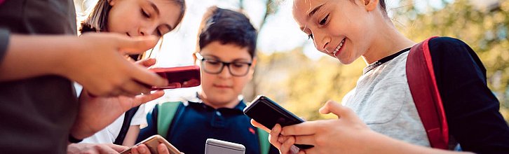 Vier Jugendliche stehen beisammen und schauen auf ihre Smartphones.