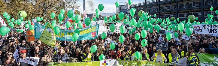 Eine große Menschenmenge auf einer Demo hält Plakate, Bannern und Luftballons in die Höhe