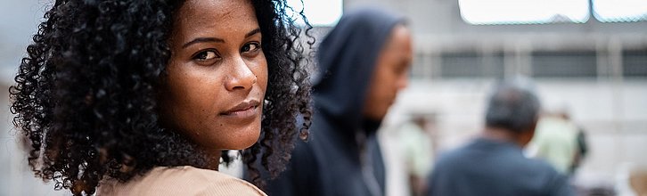 Eine Frau schaut in die Kamera. Andere Menschen sind im Hintergrund zu sehen