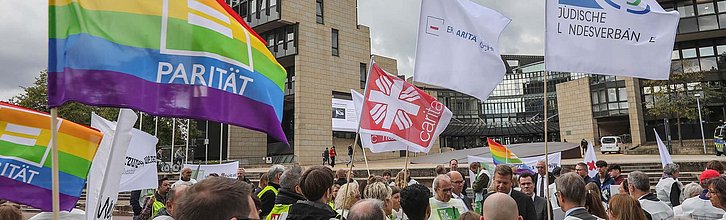 Menschen stehen mit Flaggen von verschiedenen Wohlfahrtsverbänden vor dem Landtag von NRW